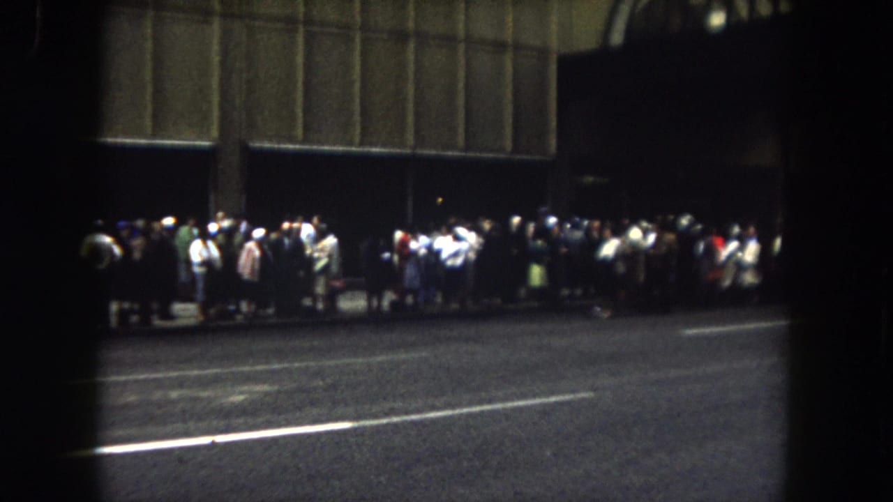 1962 Summit County, Colorado view of people gathered along a night street, filmed from across the road on 8mm.