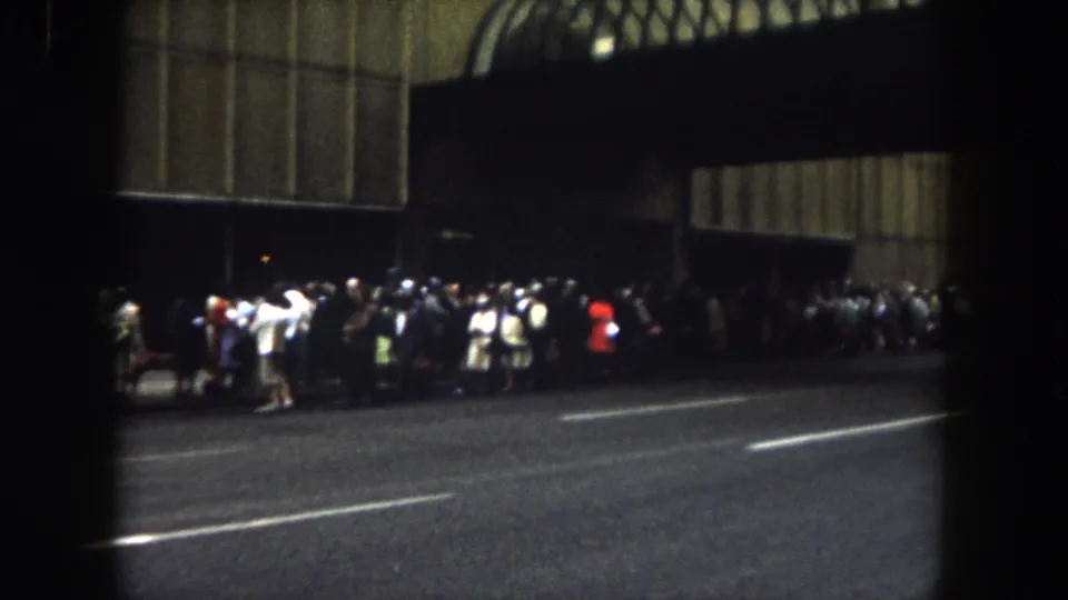 1962 Summit County, Colorado home-movie frame showing people standing along a night street near a shadowed facade.