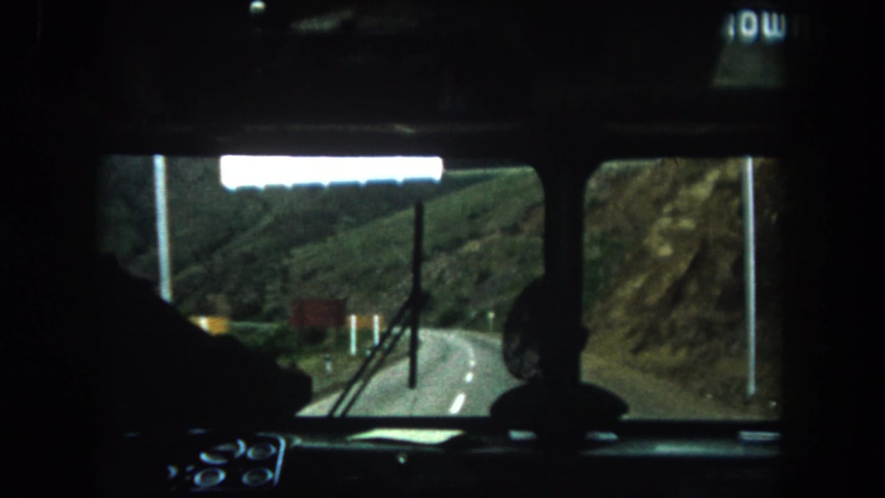 View through a bus windshield toward a curving mountain road.