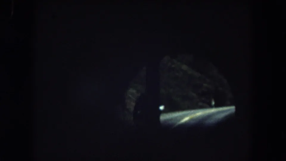 1962 Summit County bus passenger view showing a dim winding road, roadside trees, and windshield framing after leaving the tunnel.