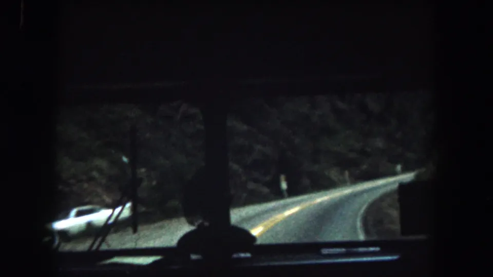 Passenger view from a 1962 bus in Summit County, Colorado, looking onto a curving mountain road bordered by trees and hillside.