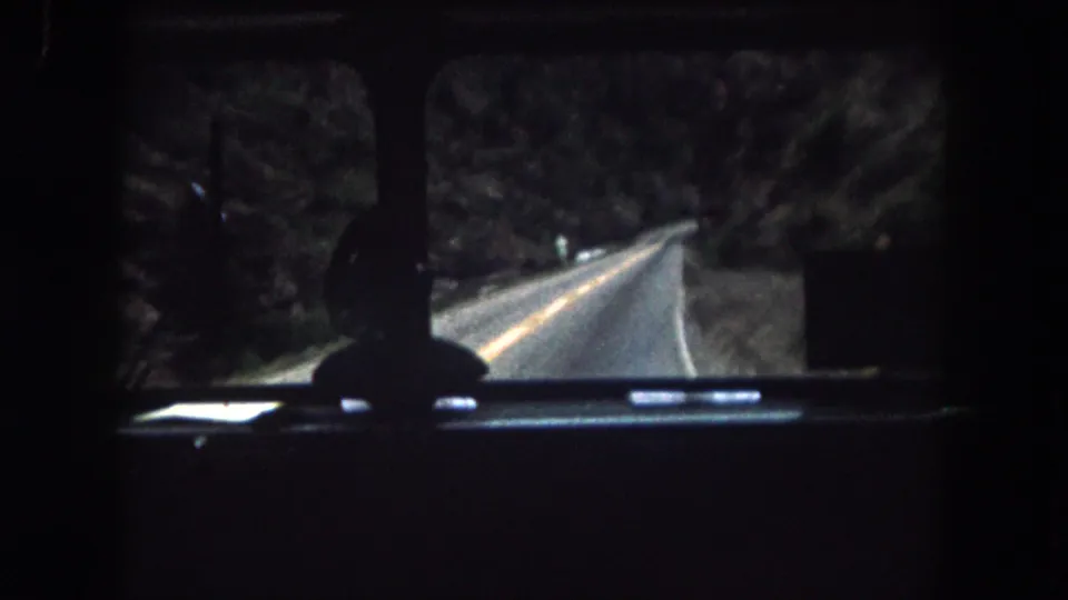 Windshield view from a 1962 Colorado vehicle interior, with a narrow road bending through trees and rocky terrain.