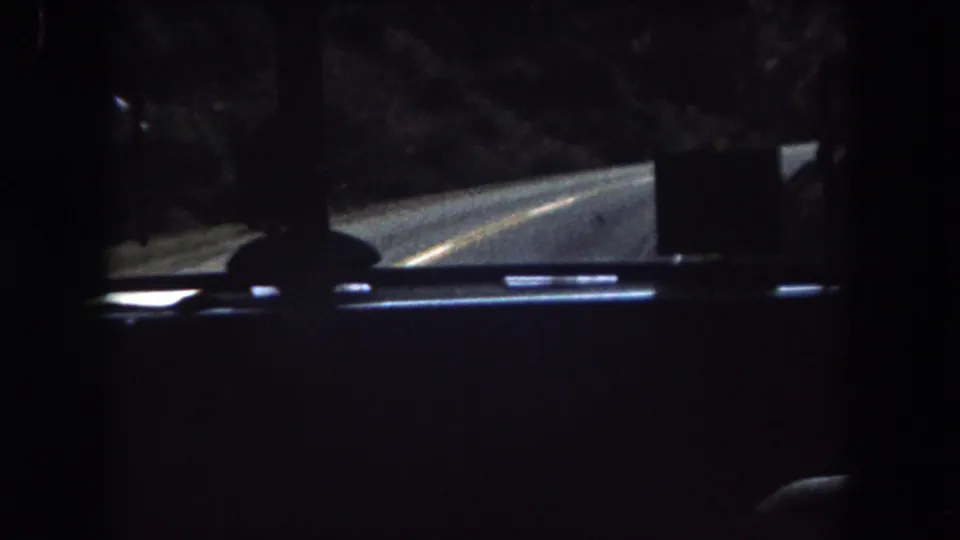 Home-movie frame from inside a vehicle in Summit County, Colorado, with the road visible beyond the dark cab interior.