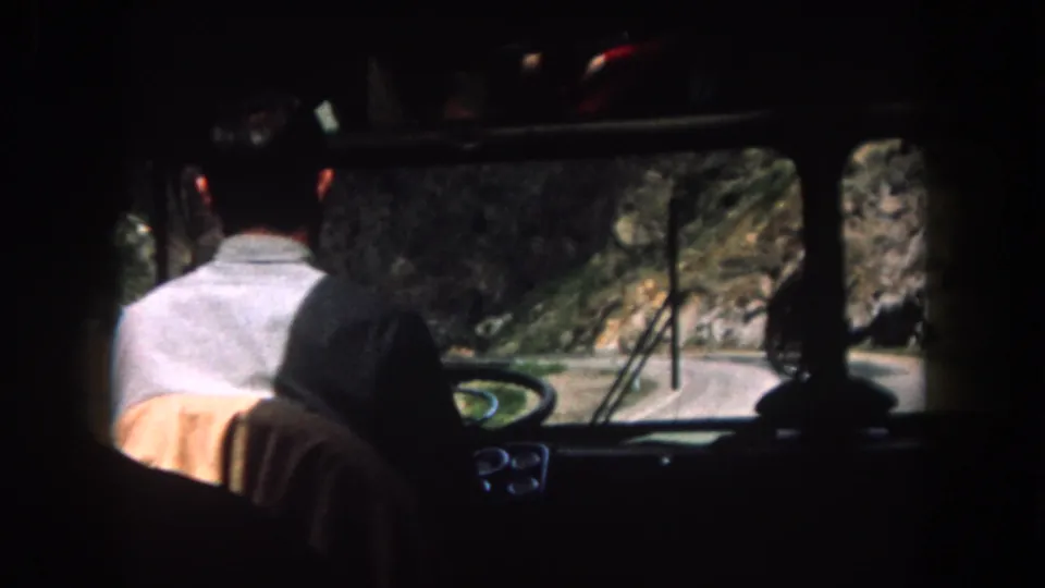 1962 Colorado vehicle interior with a driver in a light shirt seen from behind while steering along a mountain road.