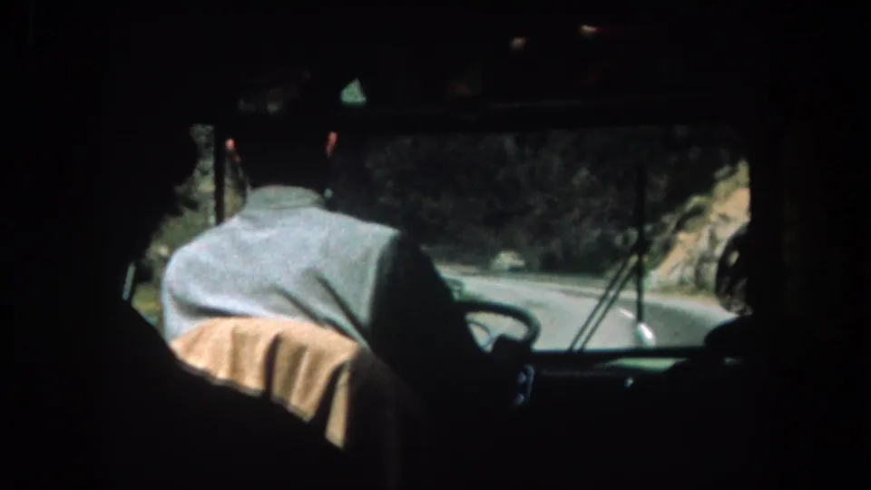 1962 Summit County, Colorado home-movie frame showing a bus driver from behind as the vehicle follows a narrow mountain road.