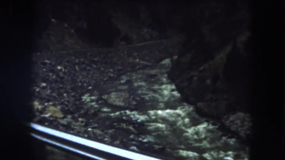 Passenger-side view from a 1962 Summit County bus ride, showing guardrail, rocks, and shaded mountain roadside.