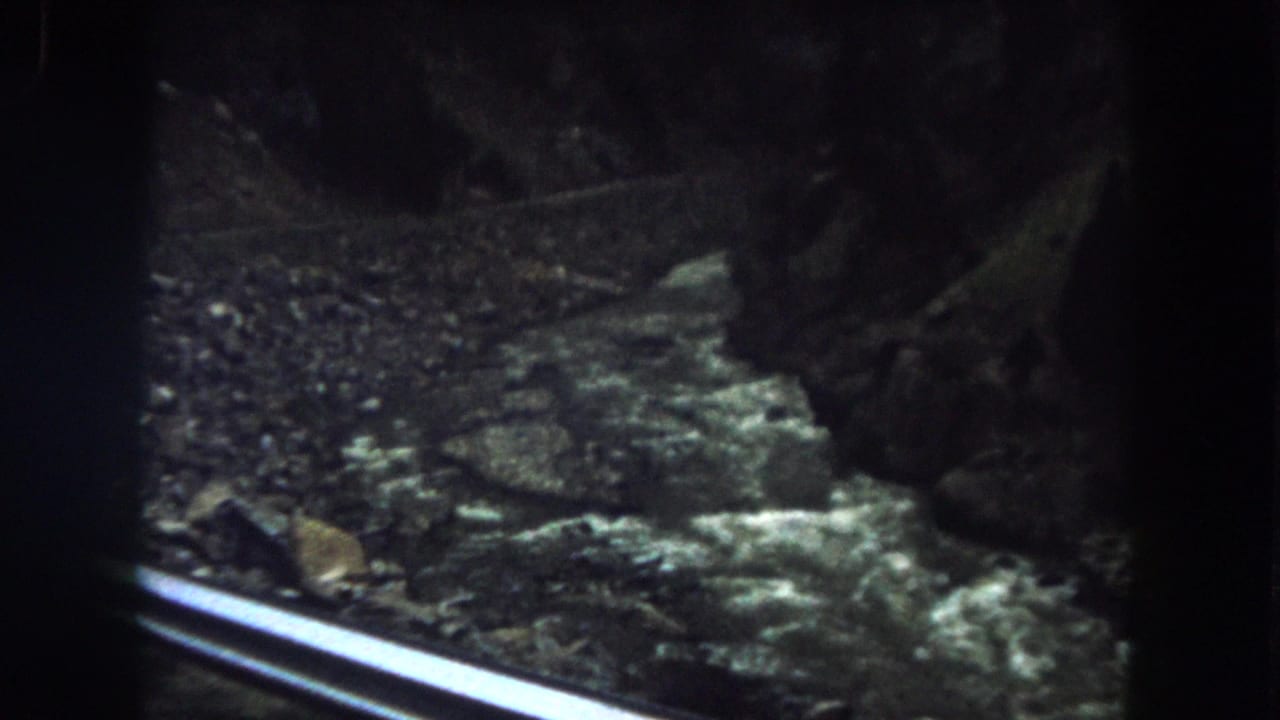 1962 8mm view of a fast river running through a rocky canyon in Summit County, Colorado, with a rail crossing the foreground.