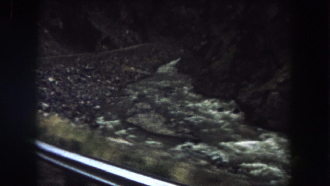 The river appears below a roadside or railway rail as the 1962 Colorado travel footage moves along the canyon.