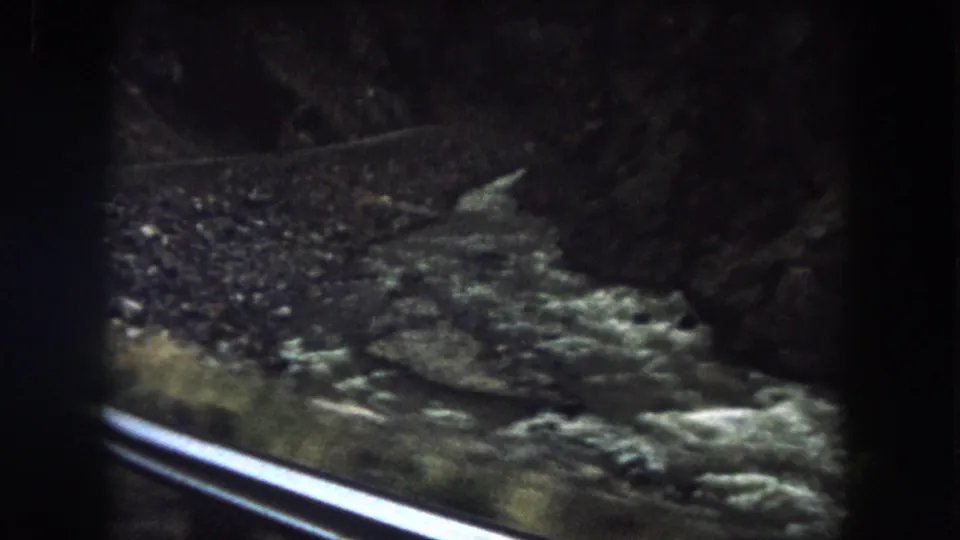 The river appears below a roadside or railway rail as the 1962 Colorado travel footage moves along the canyon.