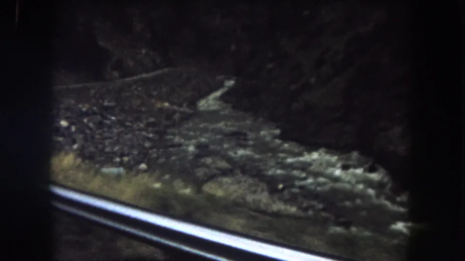 A handheld 8mm frame shows the canyon river and stony bank from a moving vehicle in Summit County, Colorado.