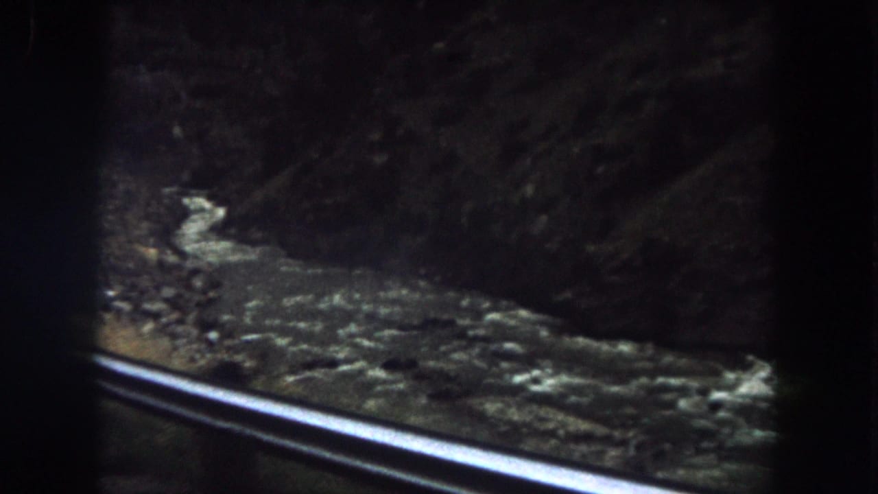 Moving-vehicle view in Summit County, Colorado, with a bright guard rail crossing the foreground and turbulent water below.