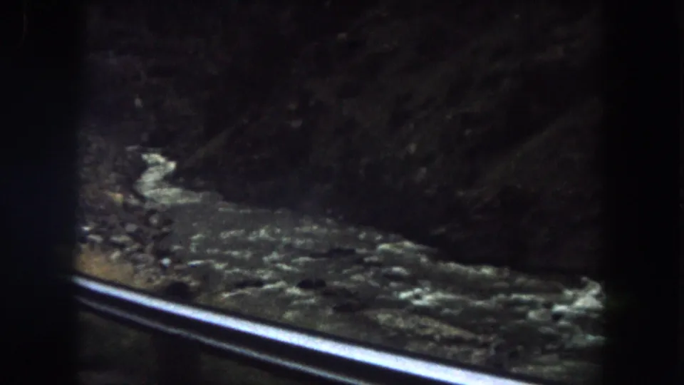 Moving-vehicle view in Summit County, Colorado, with a bright guard rail crossing the foreground and turbulent water below.