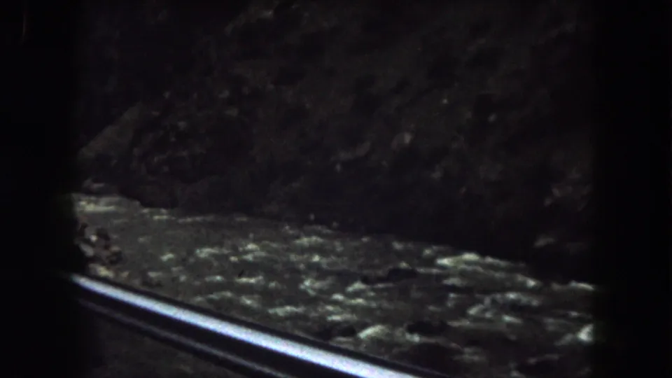 Final frame of the 1962 Colorado roadside view, with a metal guard rail in front of fast-moving water and steep dark banks.