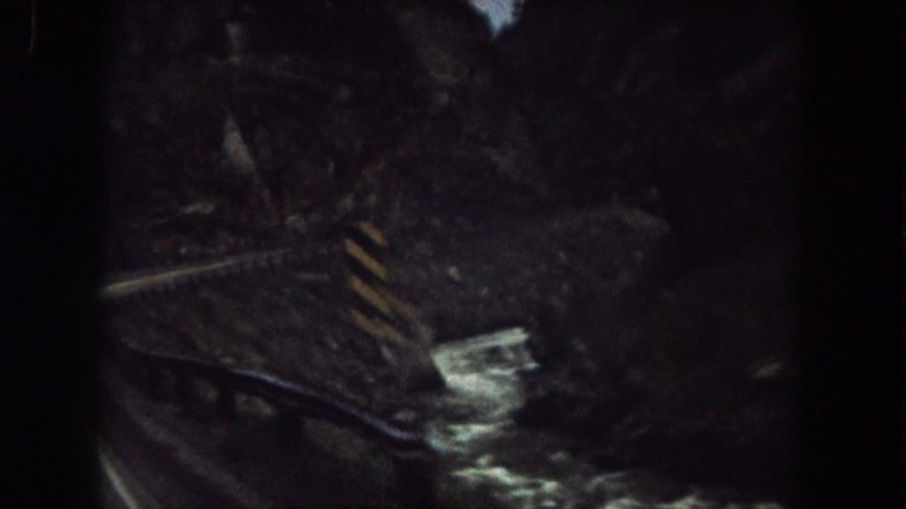1962 Summit County, Colorado home-movie frame showing a curved railway beside a narrow stream in a shadowed rocky canyon.