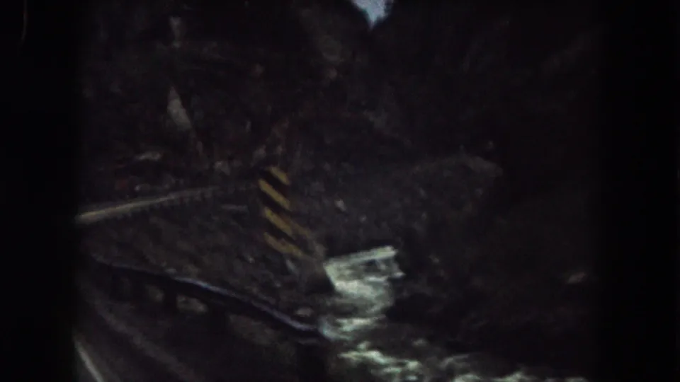 1962 Summit County, Colorado home-movie frame showing a curved railway beside a narrow stream in a shadowed rocky canyon.