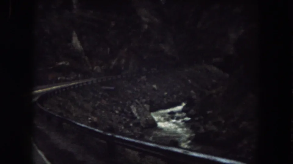1962 Colorado train-window view with a curved rail line, rocky embankment, and bright stream water in a canyon.