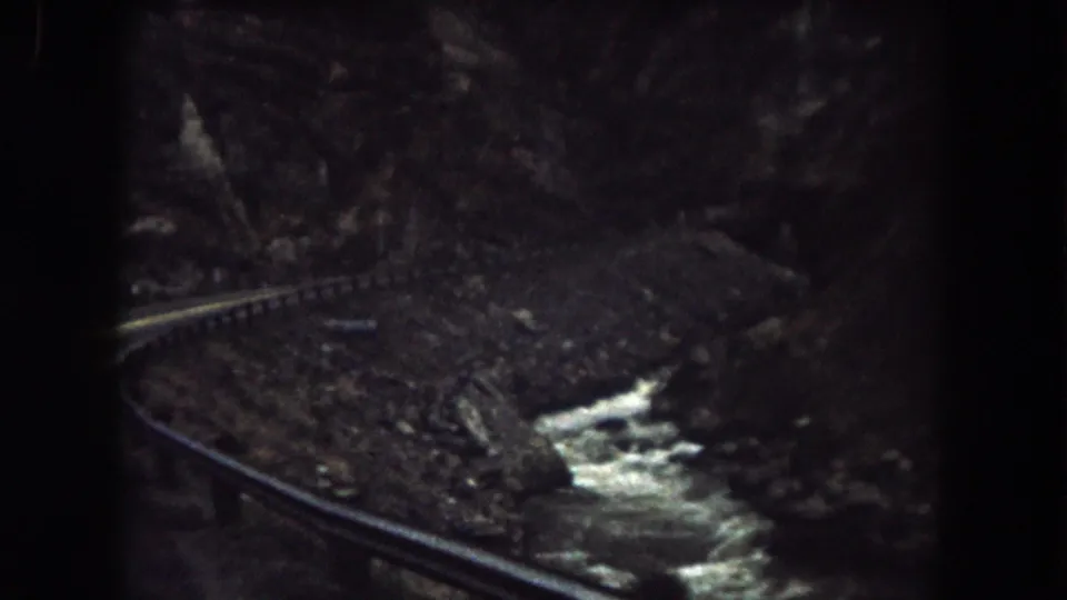 Summit County, Colorado 8mm frame showing a dark window-framed view of railway track, rocks, and a narrow stream.