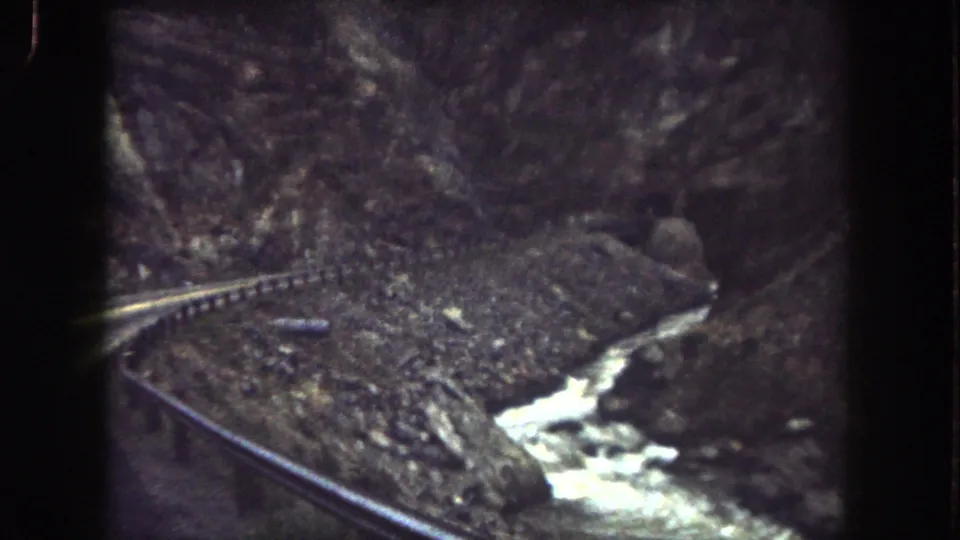 1962 Summit County train-ride frame with track along a rocky canyon and bright water cutting through the lower right.