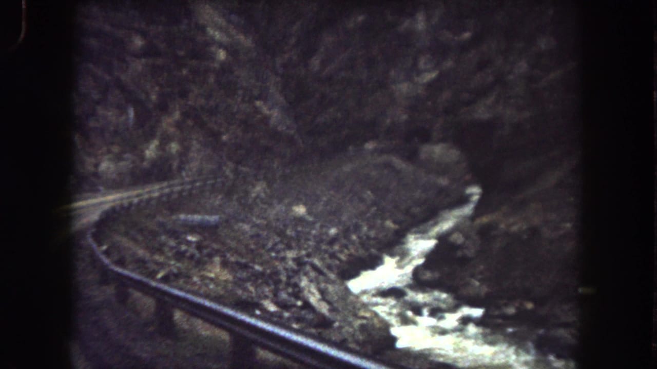 1962 Summit County, Colorado 8mm frame showing a winding canyon road, metal guardrail, rocky slope, and rushing stream.