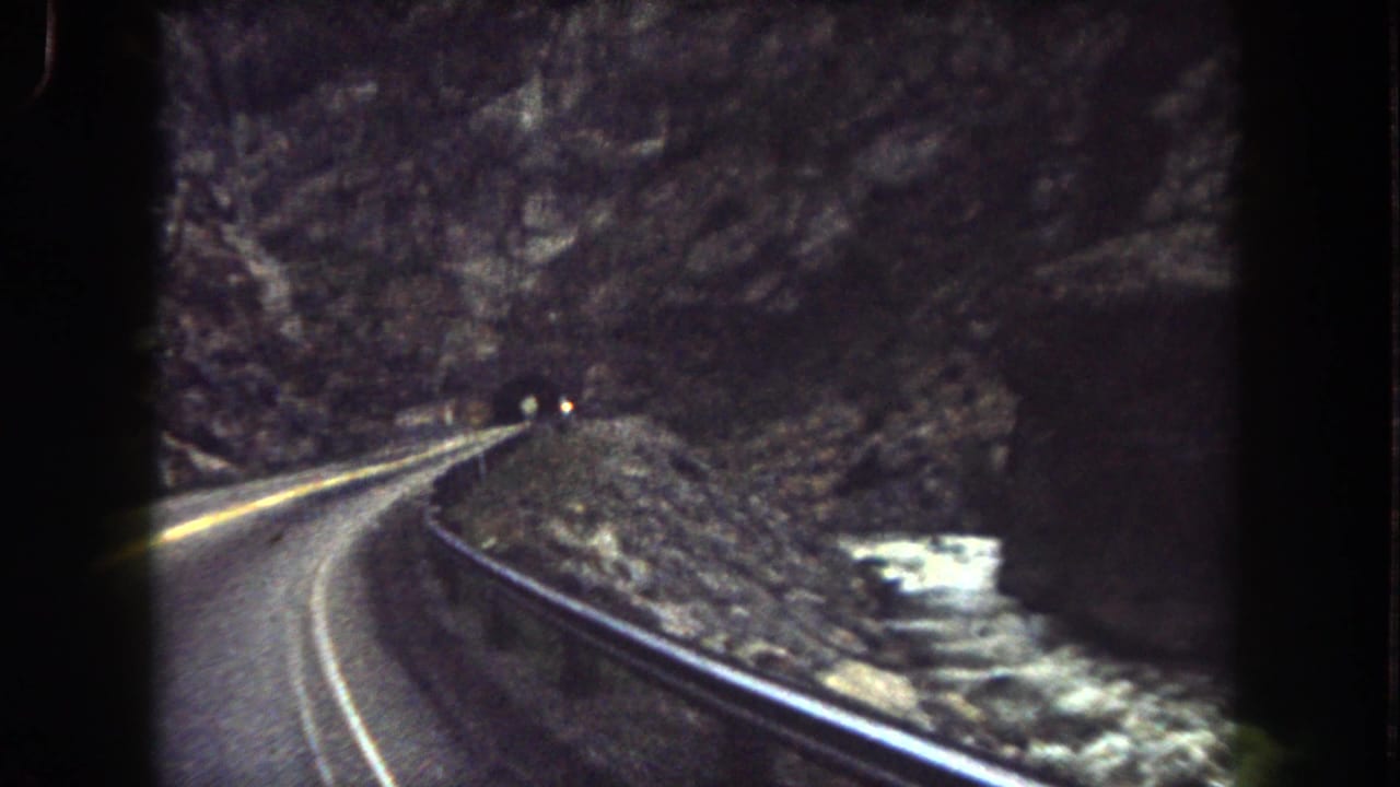 View from a moving vehicle on a Summit County mountain road, with guardrail, canyon wall, and tunnel approach visible.