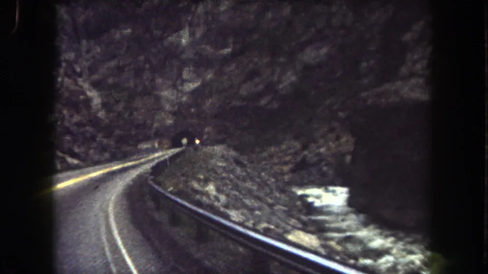 View from a moving vehicle on a Summit County mountain road, with guardrail, canyon wall, and tunnel approach visible.