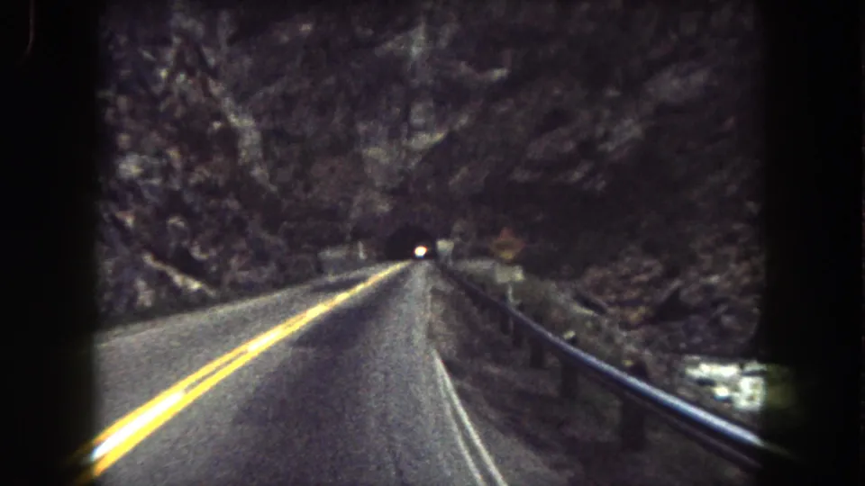 1962 8mm road-view frame in Summit County showing a two-lane highway leading toward a dark tunnel in a rocky canyon.