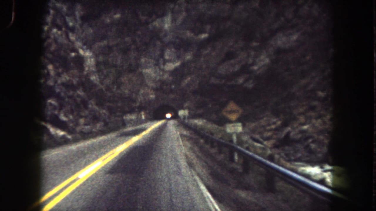 Two-lane mountain road with yellow center lines leading toward a dark tunnel opening.