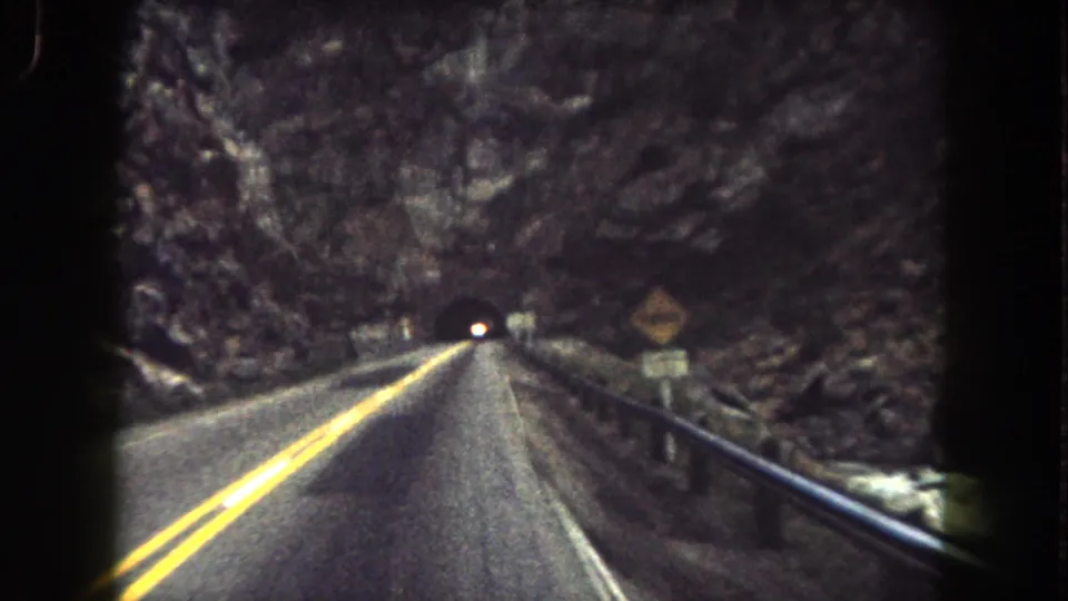 1962 8mm view from a vehicle on a Summit County mountain road approaching a tunnel through rocky terrain.
