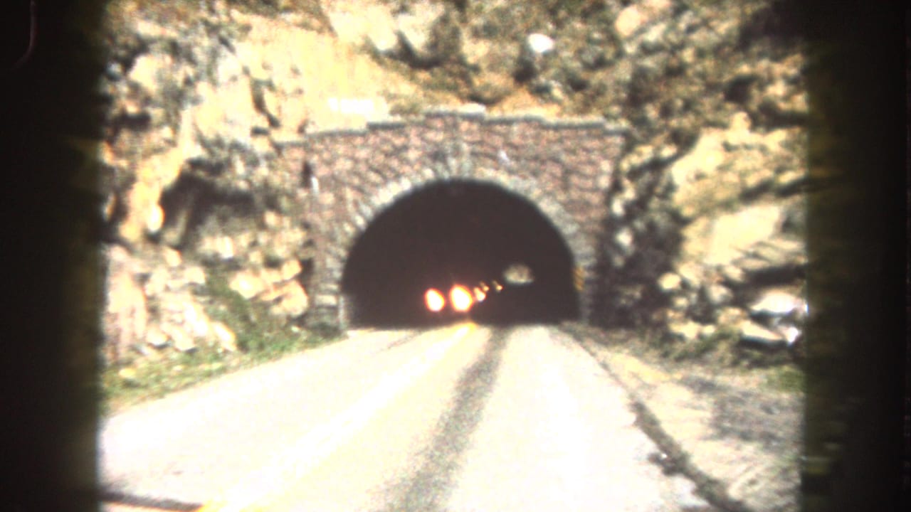 Stone-arch tunnel entrance on a mountain road with oncoming headlights inside.