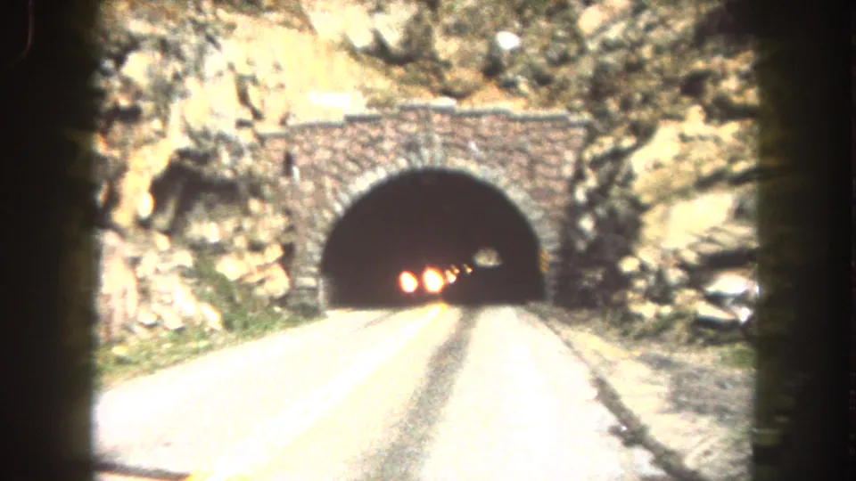 Summit County road view shows a stone-arch tunnel portal with oncoming headlights emerging from the dark opening.