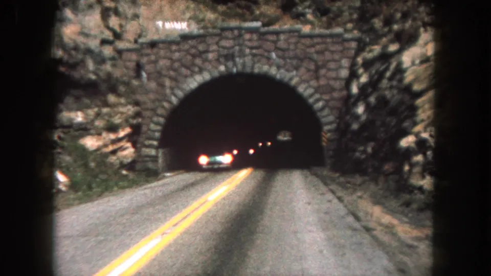 First-person 8mm road footage shows an oncoming car leaving a mountain tunnel in Summit County, Colorado.