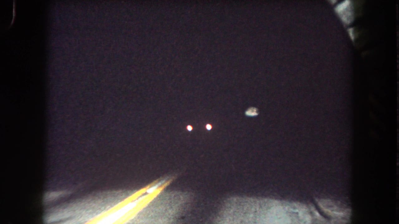 Interior tunnel view from 1962 Colorado road-trip footage, with yellow center lines fading into darkness and distant lights ahead.