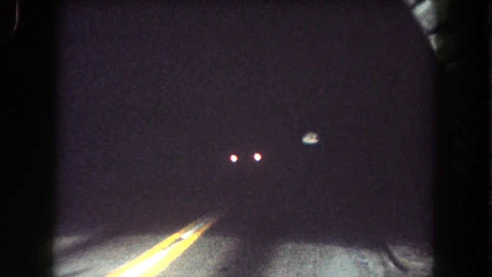 Interior tunnel view from 1962 Colorado road-trip footage, with yellow center lines fading into darkness and distant lights ahead.