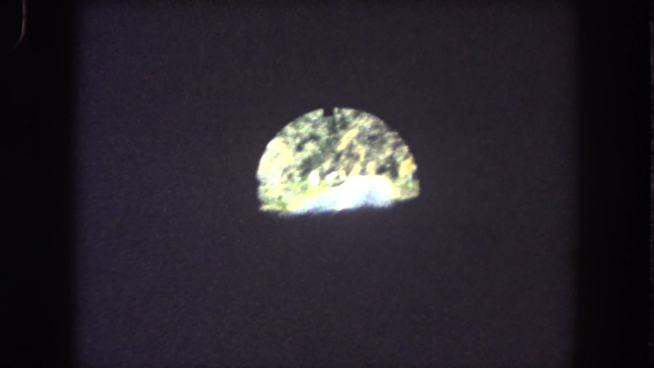 1962 8mm vehicle POV inside a dark Summit County tunnel, with a bright arched exit and faint mountain road visible beyond.