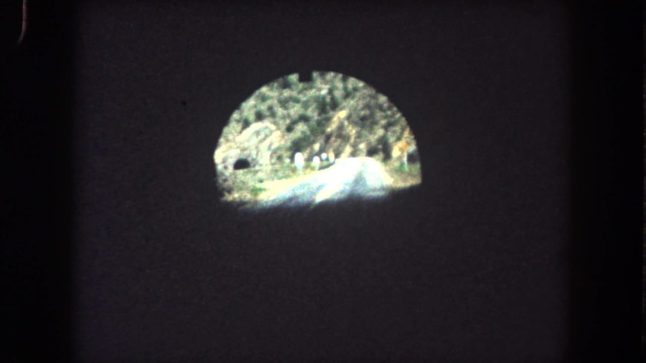 Vehicle POV from a dark tunnel in Summit County, Colorado, looking toward a sunlit mountain road, rocky hillside, and trees.