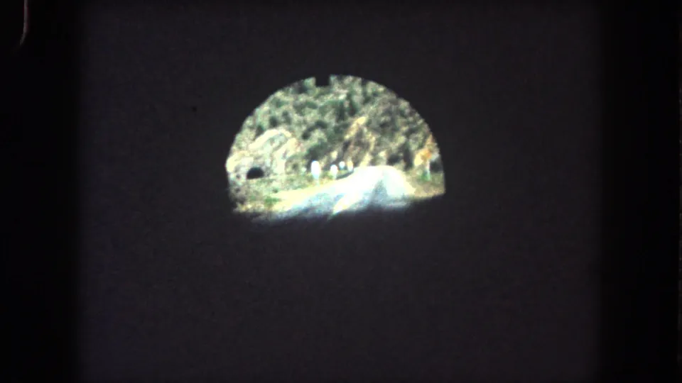 Vehicle POV from a dark tunnel in Summit County, Colorado, looking toward a sunlit mountain road, rocky hillside, and trees.