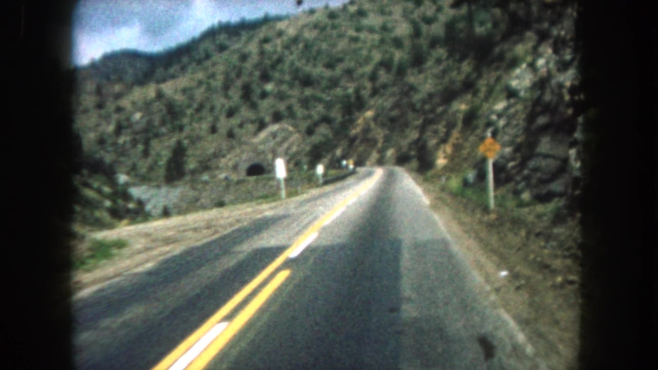 Vehicle-mounted or passenger-shot 8mm view of a Summit County mountain road curving toward a small tunnel entrance in 1962.