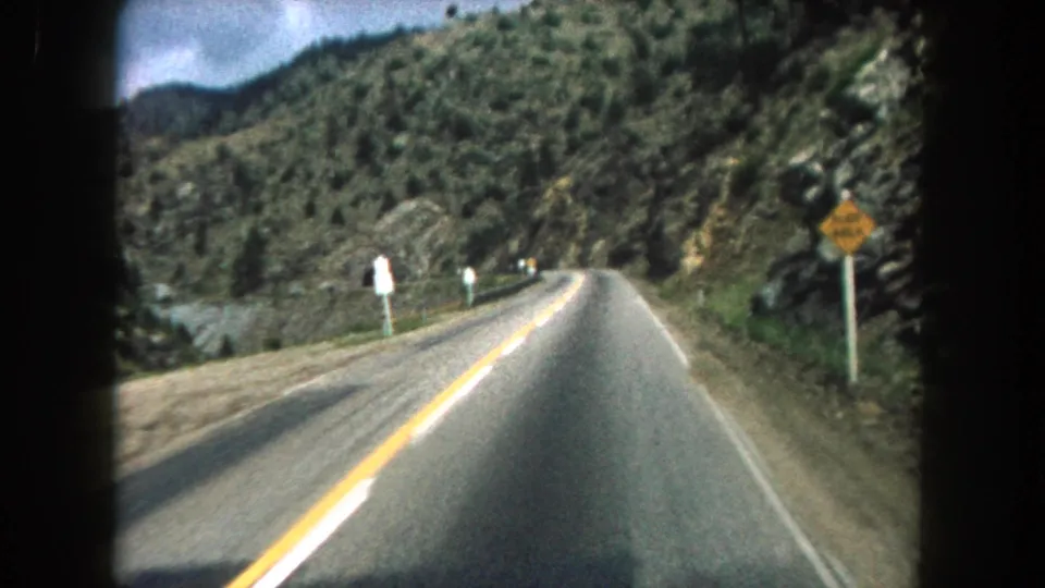 Summit County, Colorado driving POV on 8mm film, with roadside signs, yellow center lines, and rocky mountain slopes visible.