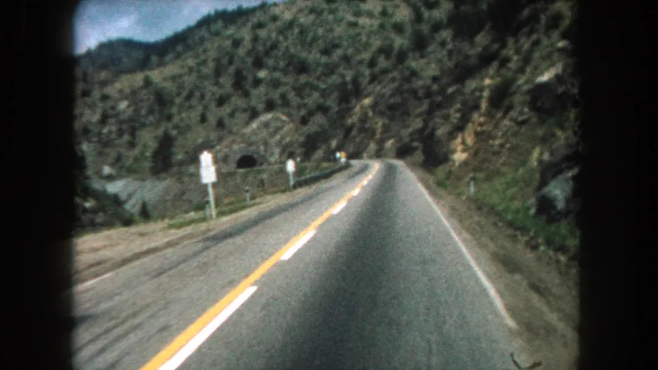 1962 8mm vehicle POV in Summit County, Colorado, showing a narrow road leading toward a dark tunnel opening in the mountains.