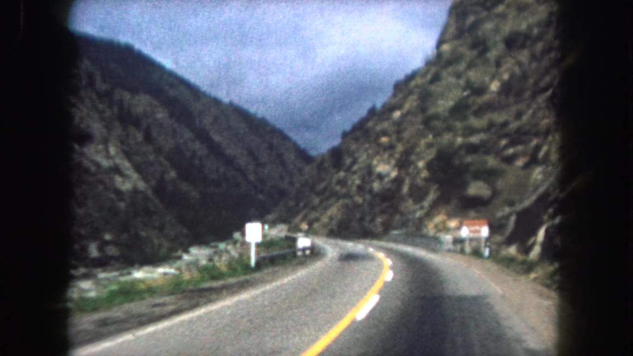 1962 8mm view of a two-lane road through steep Summit County, Colorado mountain terrain, filmed from a moving vehicle.