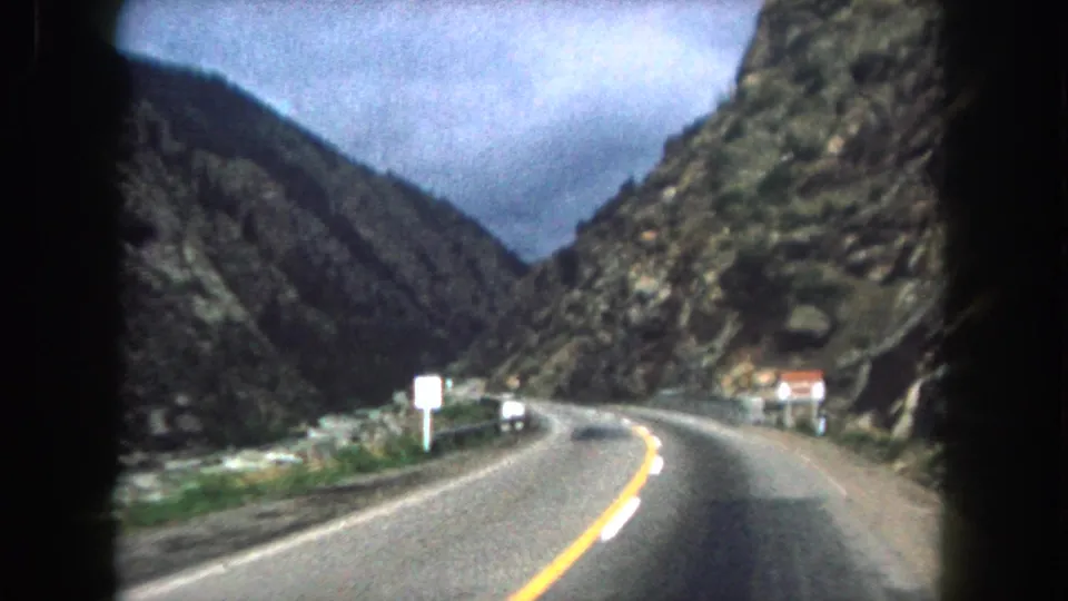 1962 8mm view of a two-lane road through steep Summit County, Colorado mountain terrain, filmed from a moving vehicle.
