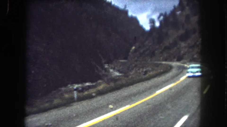 1962 Colorado road-trip frame with a pale car partly near the edge of the shot on a curving mountain highway.