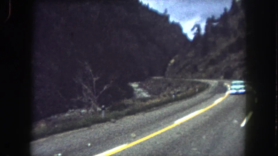 Final Summit County road frame showing the pale car farther along the bend in grainy 8mm color footage.
