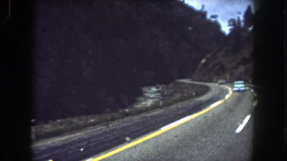 1962 Summit County, Colorado 8mm road scene showing a car farther ahead on a winding highway beside a river and steep wooded hillside.