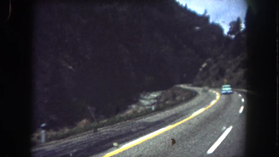 Final 1962 Summit County, Colorado frame with a small car on a mountain road, river at left, and forested slopes around the curve.