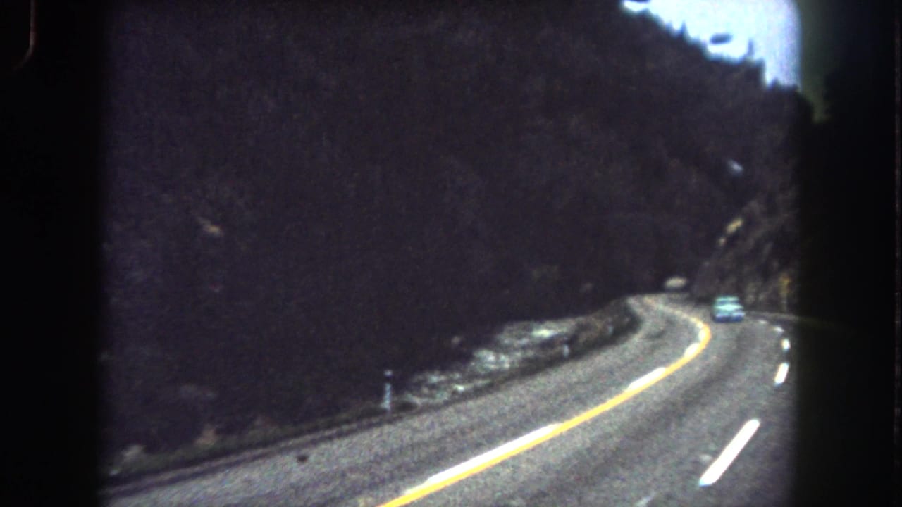 Mountain highway view in Summit County, Colorado, with a car ahead on a curve and dark hillsides around the road.