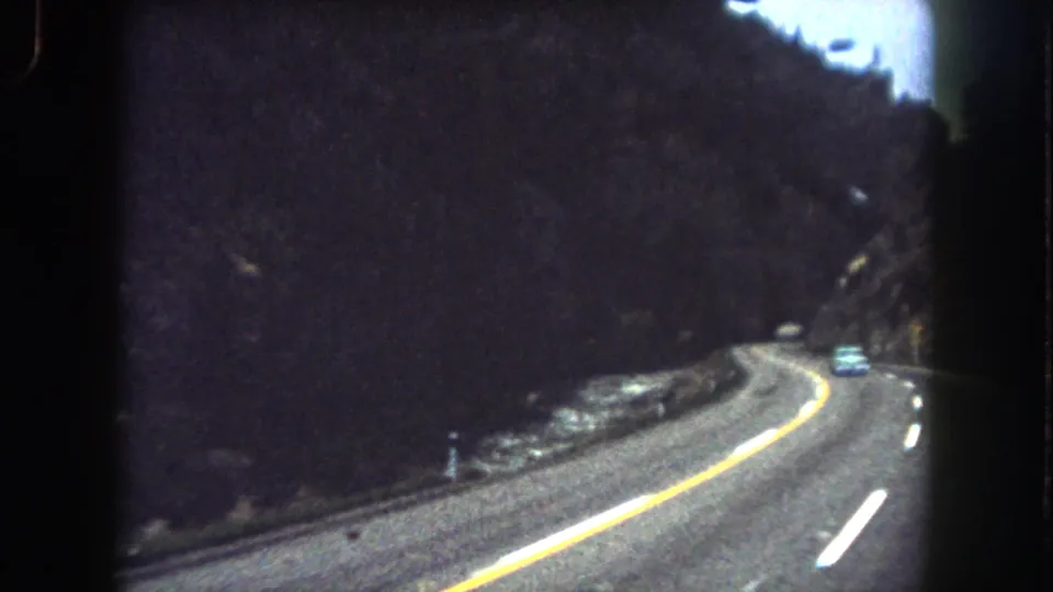 Mountain highway view in Summit County, Colorado, with a car ahead on a curve and dark hillsides around the road.