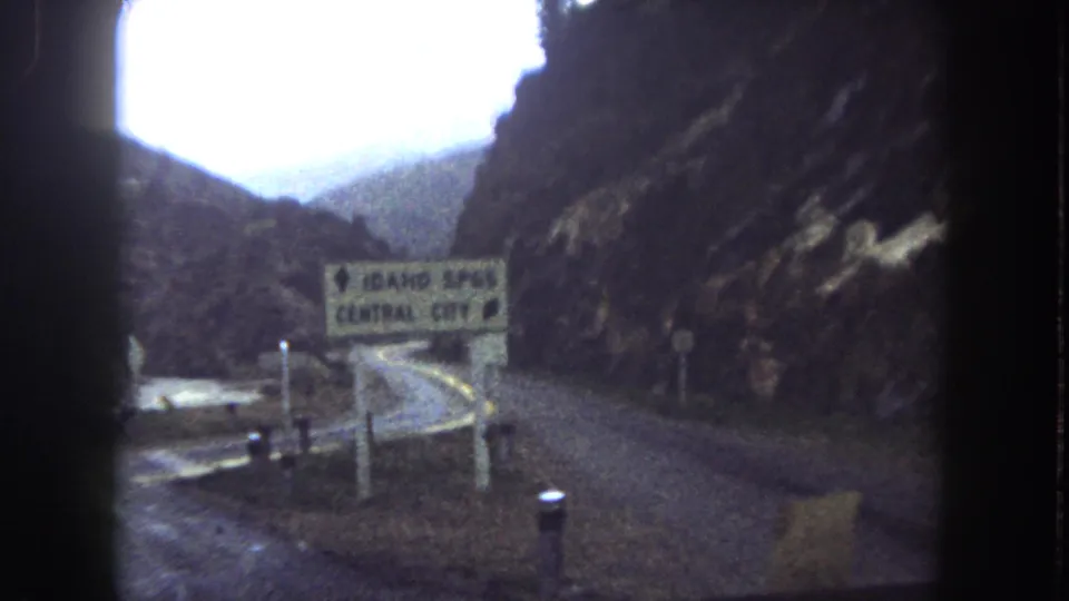 Readable Idaho Springs and Central City direction sign beside a winding Summit County mountain road in 1962 footage.