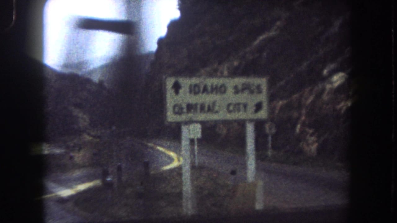 1962 8mm frame of a Colorado mountain road with a sign pointing toward Idaho Springs and Central City.