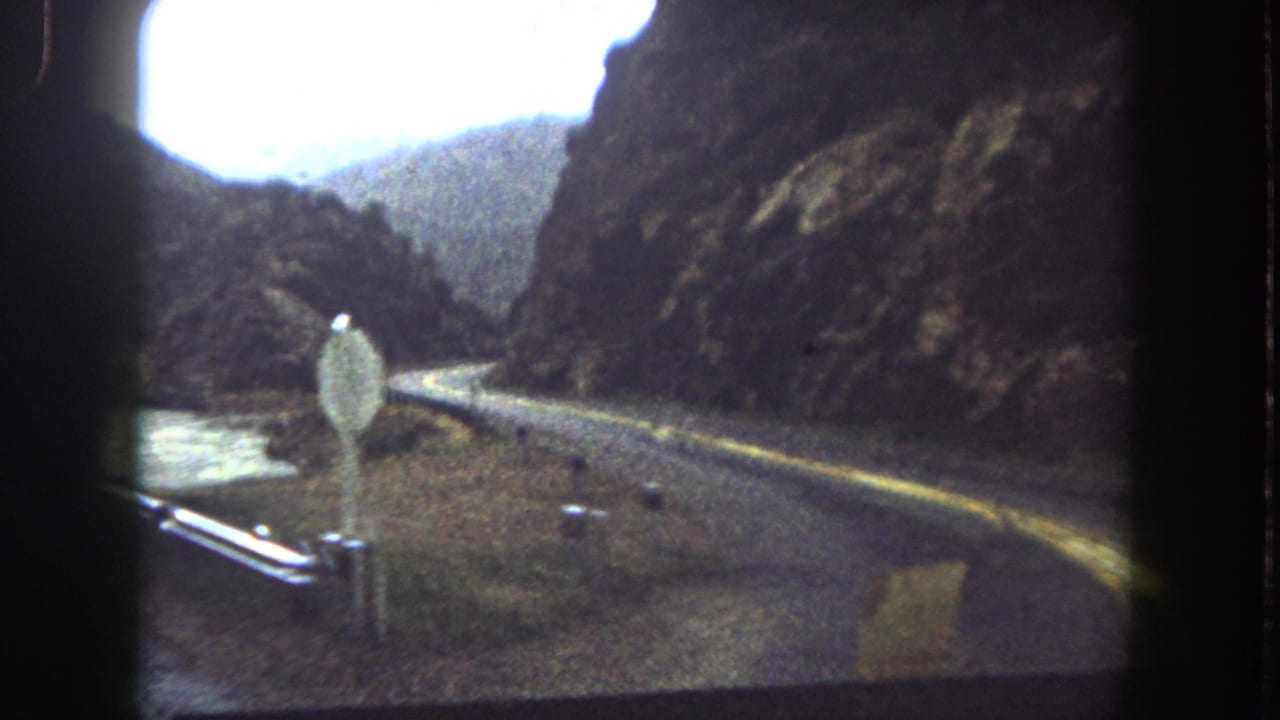 Moving-vehicle view of a Summit County mountain road curving along water with guardrails and steep rock walls.